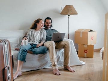 Cheerful couple watching video on laptop together while sitting on couch in living room when moving house