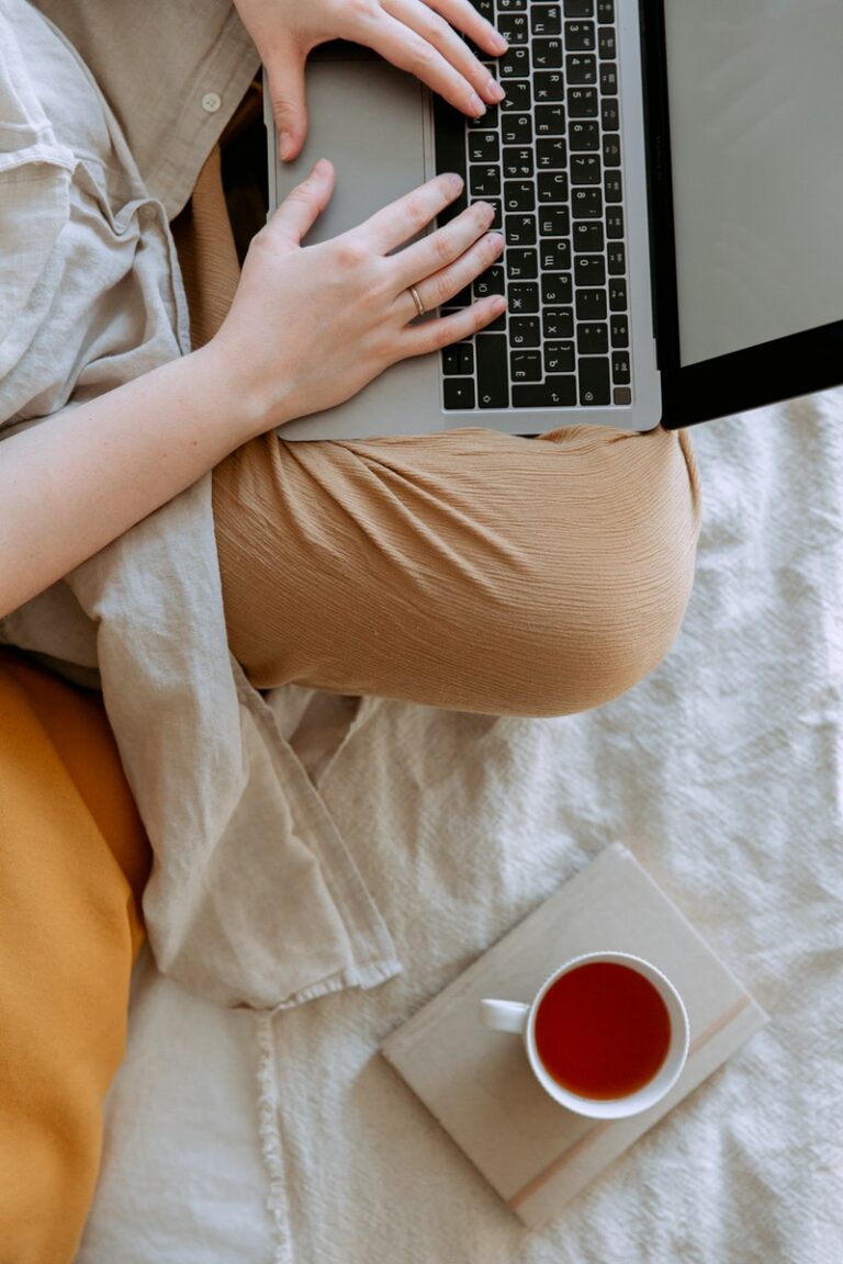 Anonymous woman in casual clothes sitting on sofa and browsing laptop with blank screen while working on project on bed