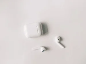 White first-generation AirPods with their charging case, on a plain background.