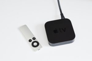 Apple TV device next to its silver remote control on a white background.