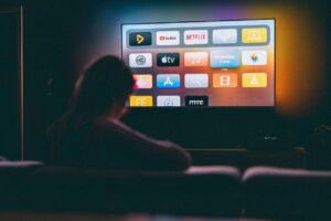 A person sitting in a dark room illuminated by the glow of a large screen displaying the Apple TV interface with various app icons