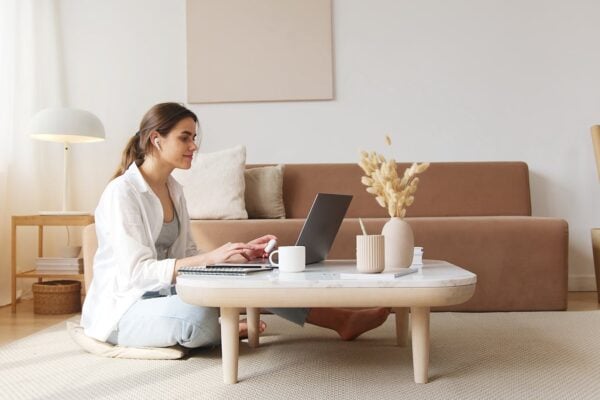 A woman uses a laptop at a coffee table in a cozy living room, embodying a relaxed work-from-home lifestyle.
