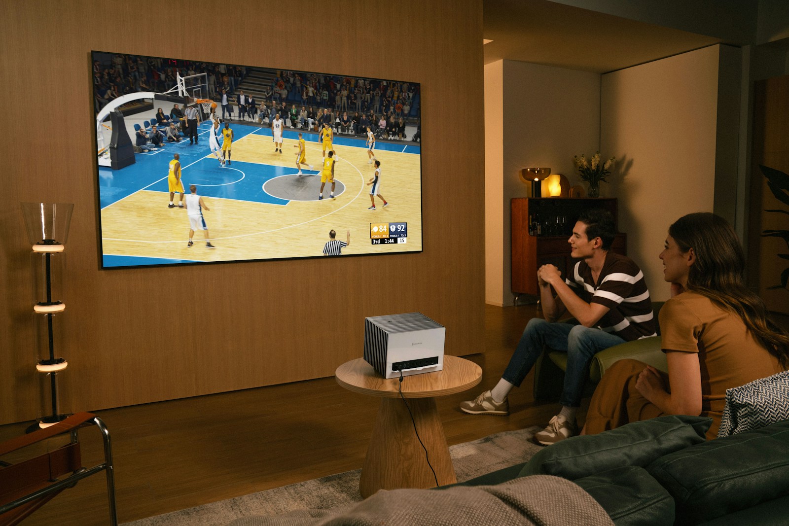 People watch a basketball game on a large screen.