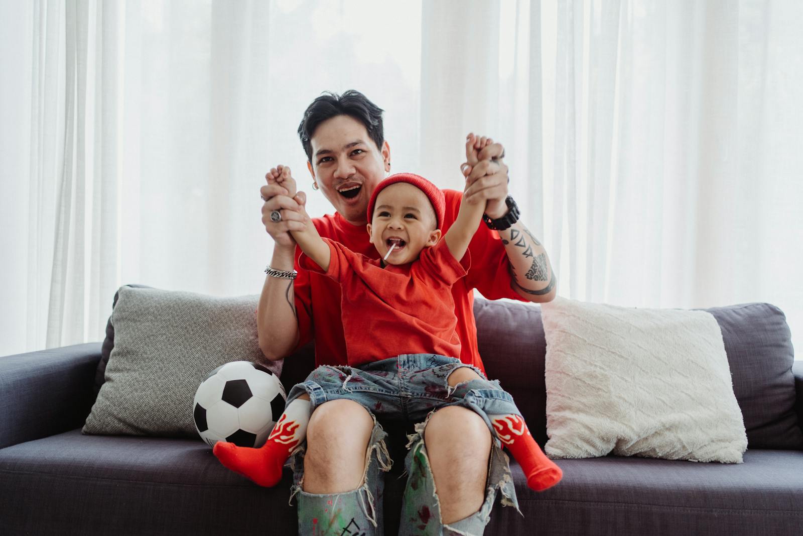 Father and son bonding on the couch, dressed in red, enjoying a football moment together.