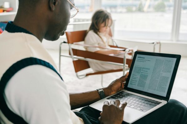 Adult man working on a laptop while a child sits in the background. Bright indoor setting.