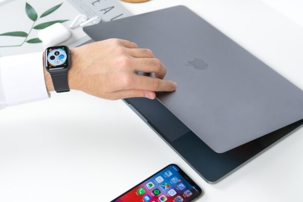 person opening gray MacBook beside iPhone on white wooden table