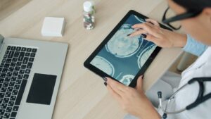 Doctor examining brain scan on tablet at desk.
