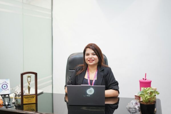 A smiling woman sits at a desk with a laptop.