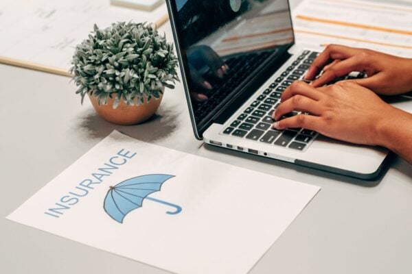 Hands typing on a laptop at a desk with an insurance paper and plant, suggesting a work environment.