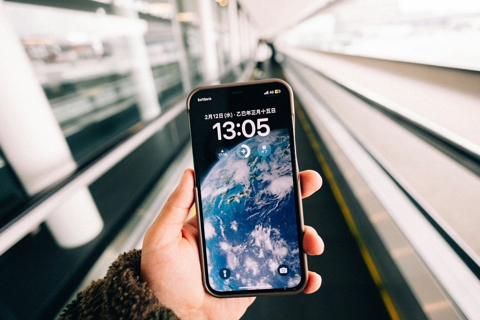 Person holding smartphone with earth wallpaper on escalator