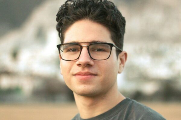 a young man wearing glasses standing in front of a mountain